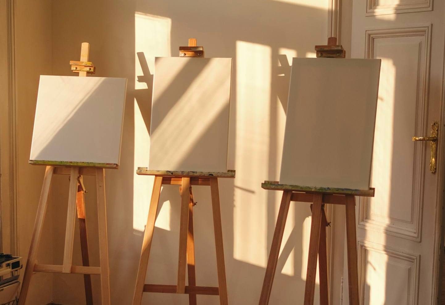 Trzy sztalugi z płótnami w złotym świetle pracowni POSTO