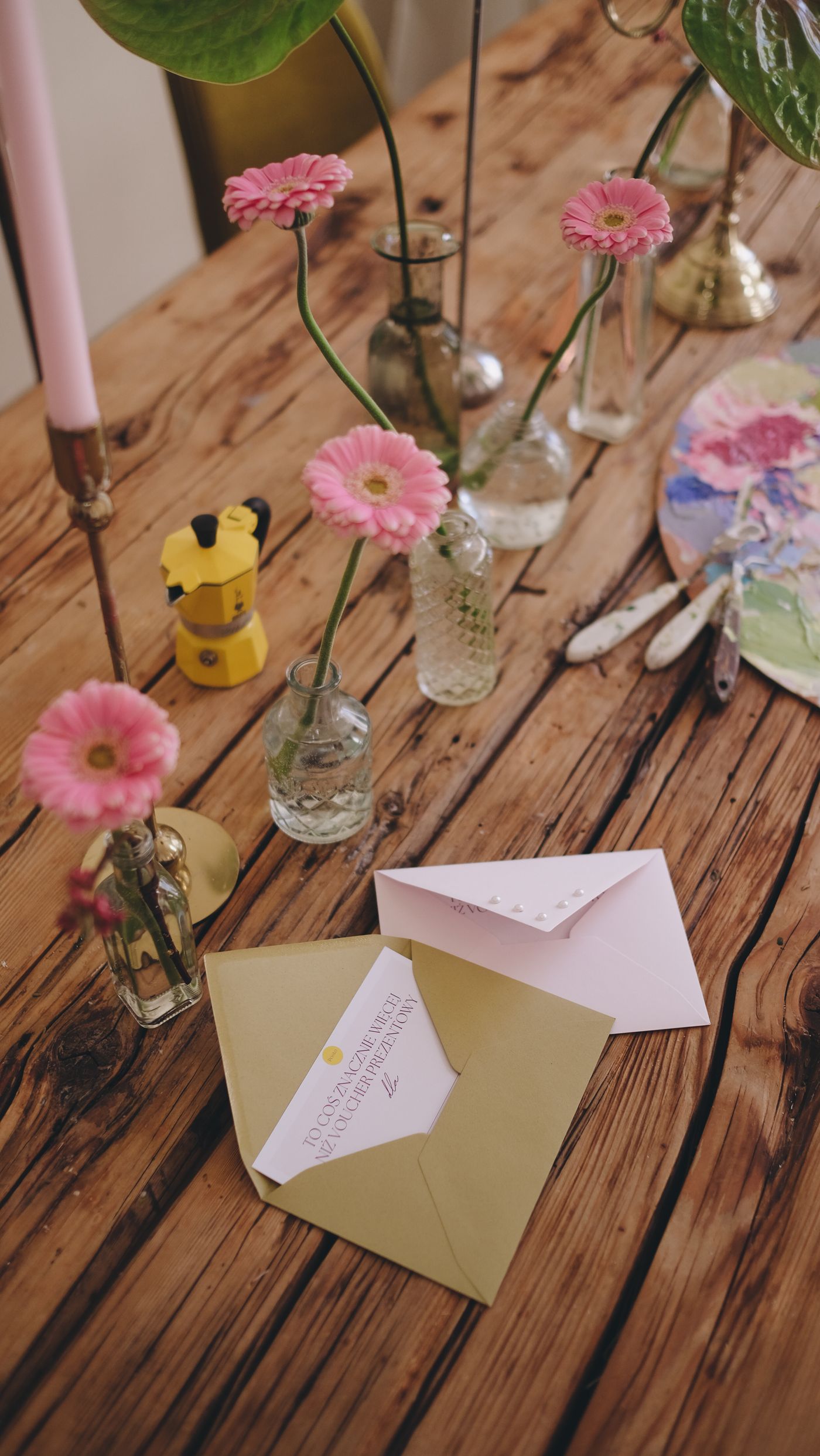 Złota koperta z voucherem POSTO na stole z różowymi kwiatami